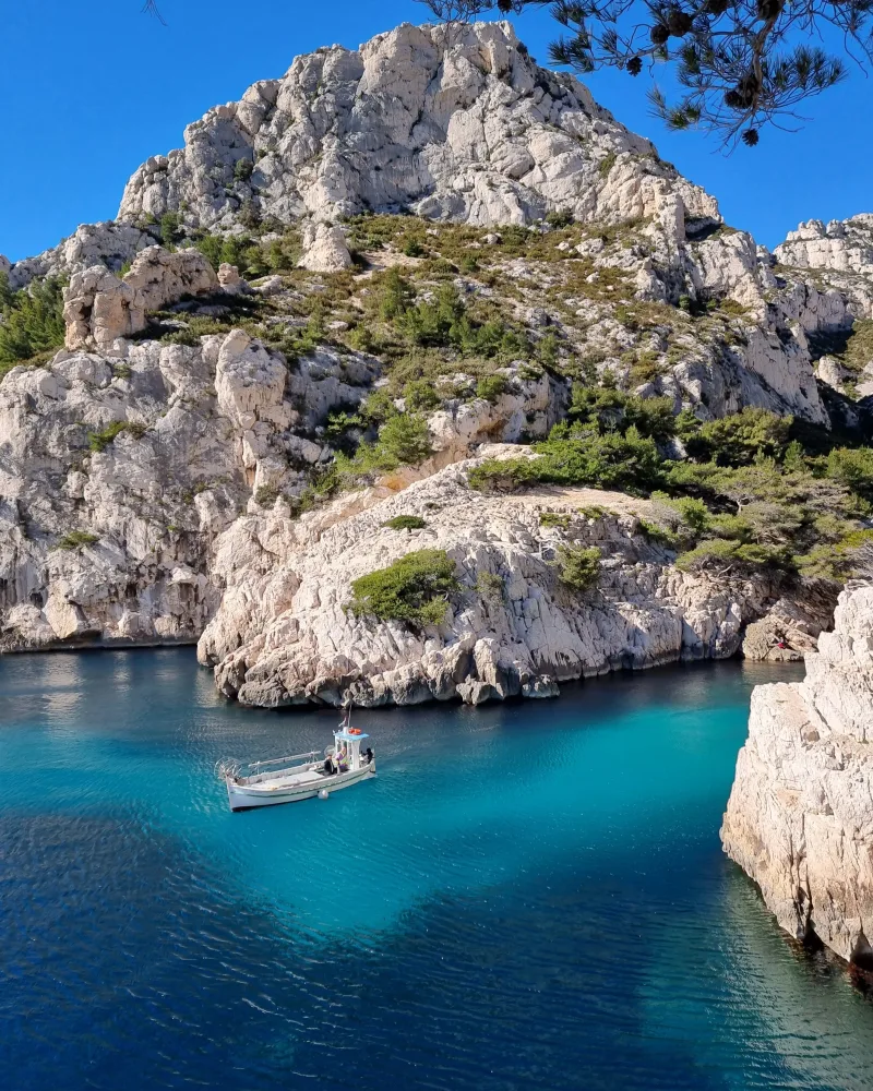 Petit bateau de pêche blanc naviguant dans les eaux turquoise d'une calanque encadrée de hautes falaises calcaires