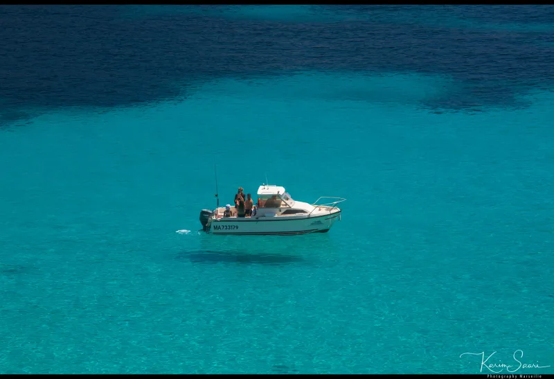 Petit bateau de pêche blanc ancré sur l'eau turquoise cristalline d'une calanque — photographie aérienne Marseille