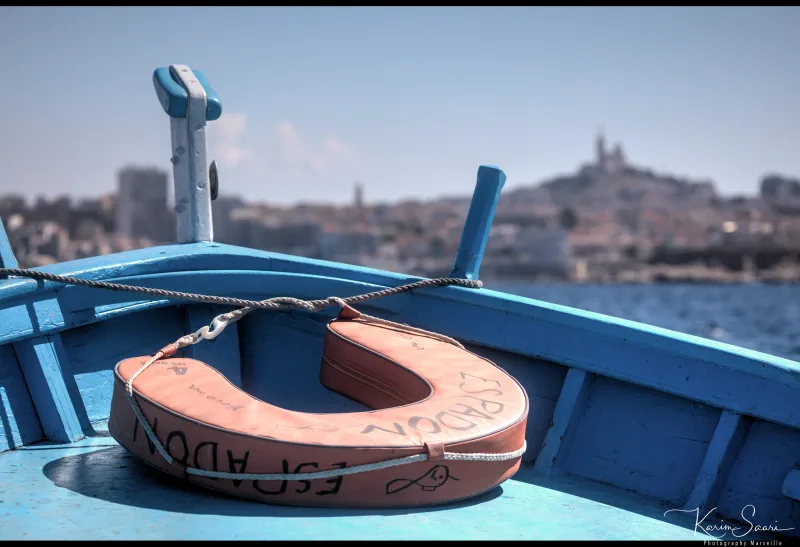 Bouée de sauvetage sur la proue d'un bateau bleu, Notre-Dame de la Garde floue en arrière-plan — Marseille
