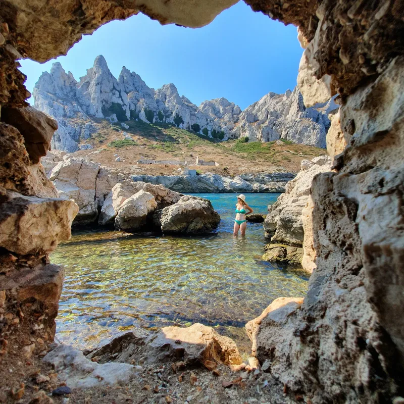 Calanque vue depuis une ouverture dans la roche, femme en bikini dans l'eau cristalline, aiguilles rocheuses en arrière-plan