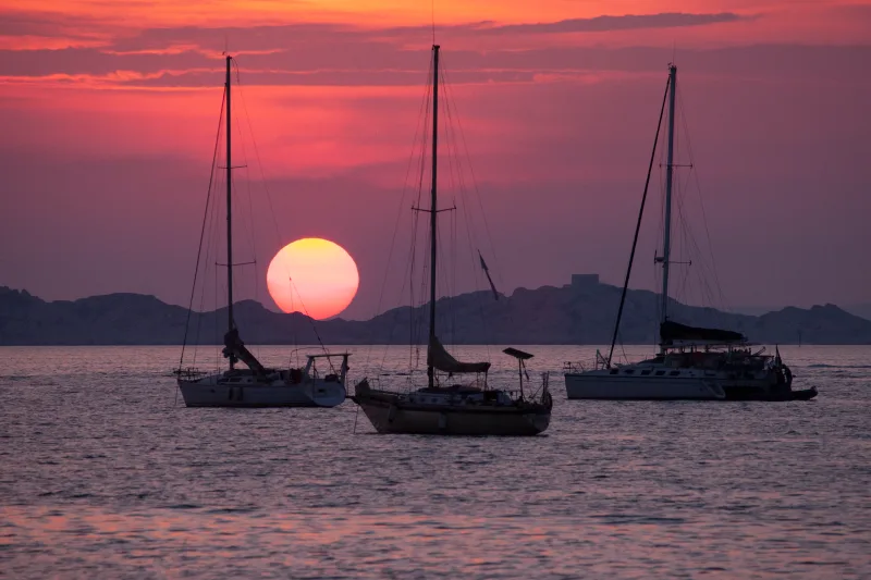 Coucher de soleil rouge sur la mer avec trois voiliers en silhouette — Méditerranée