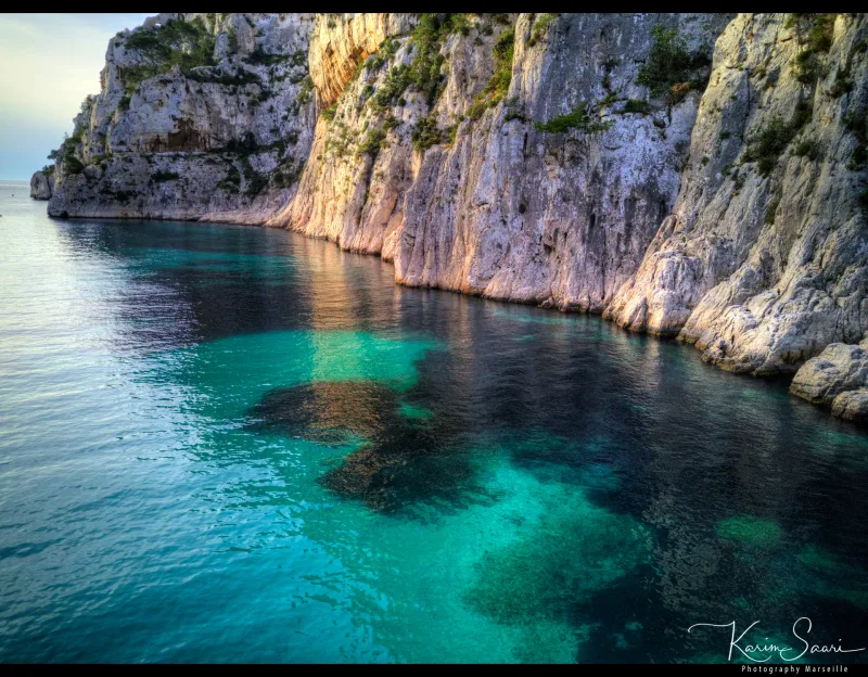 Falaises calcaires dorées se reflétant dans les eaux turquoise d'une calanque au coucher de soleil