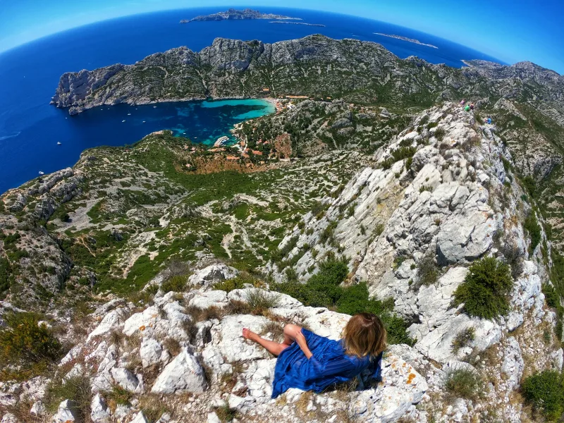 Vue fisheye depuis le sommet des Calanques, femme en robe bleue sur les rochers, anse et mer en contrebas