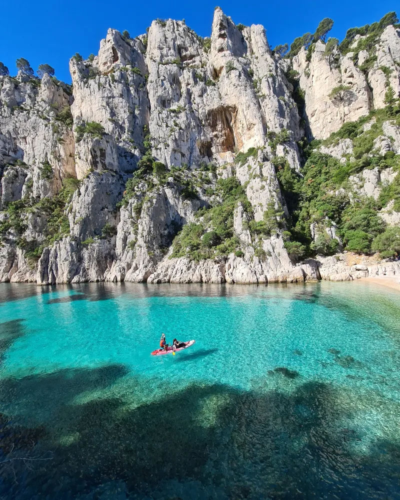 Kayakistes sur l'eau turquoise d'une calanque encadrée de hautes falaises calcaires et de pins — Calanques de Marseille