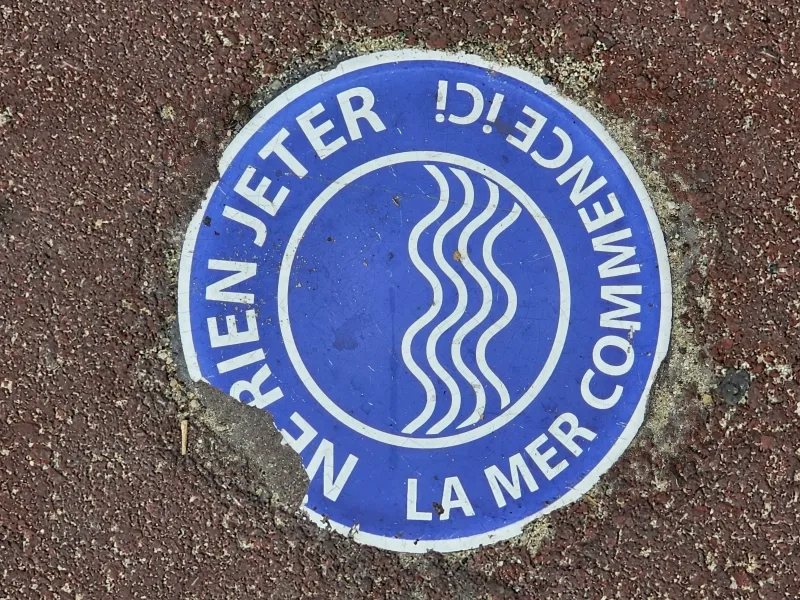 Marquage au sol "Ne rien jeter ici — La mer commence ici" sur asphalte rouge — sensibilisation à la pollution urbaine