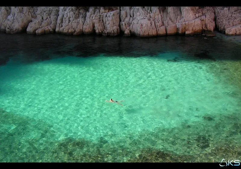 Nageur solitaire dans les eaux émeraude translucides d'une anse entre falaises de roches rouges