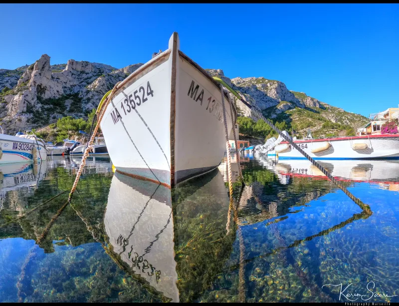 Proue d'un pointu marseillais se reflétant dans l'eau cristalline d'une calanque, cordages et fond marin visible — HDR