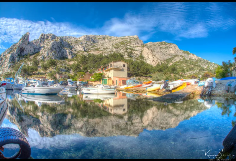 Petit port de calanque avec bateaux amarrés se reflétant dans l'eau cristalline, falaises calcaires et ciel bleu — HDR Marseille