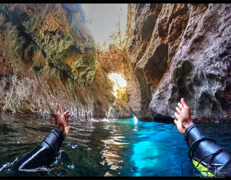 Exploration en apnée d'une grotte marine dans les Calanques de Marseille — vue subjective, mains en néoprène, eau turquoise — © Karim Saari, photographe sous-marin Marseille