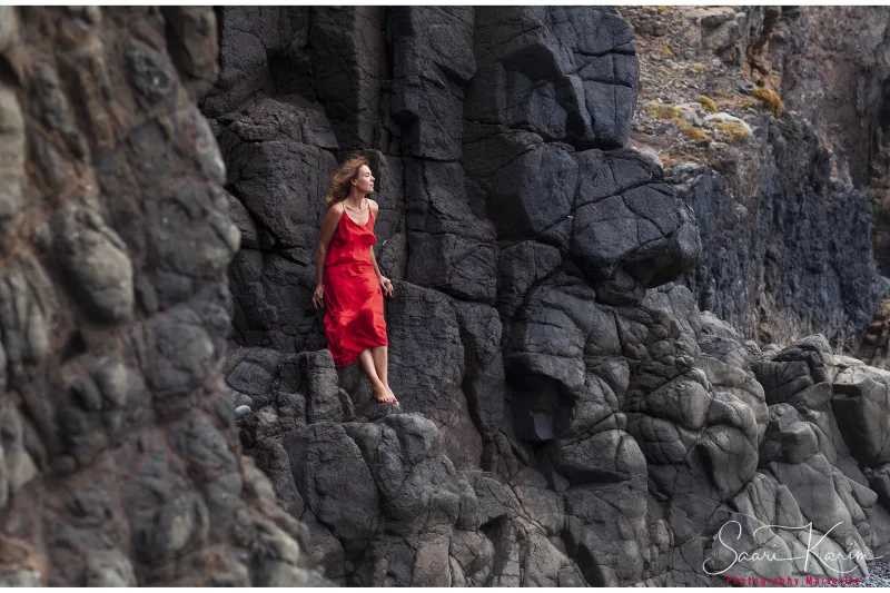 Femme en robe rouge sur des rochers volcaniques noirs, côte sauvage — photographe paysage Karim Saari