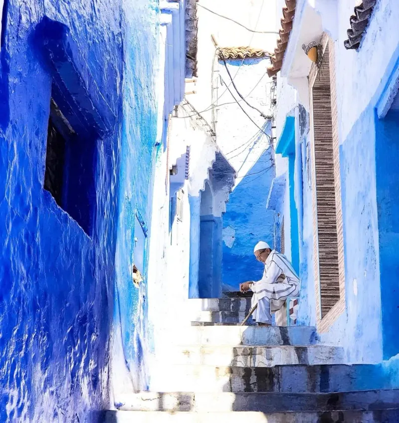 Ruelle bleue de Chefchaouen, vieil homme en djellaba sur des marches — photographe Maroc Karim Saari