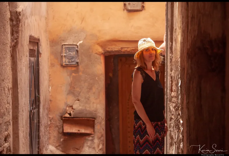 Femme au chapeau dans une ruelle de médina marocaine, murs ocre, lumière rasante — Karim Saari