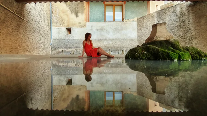 Femme en robe rouge se reflétant dans une flaque, village provençal — photographe Karim Saari